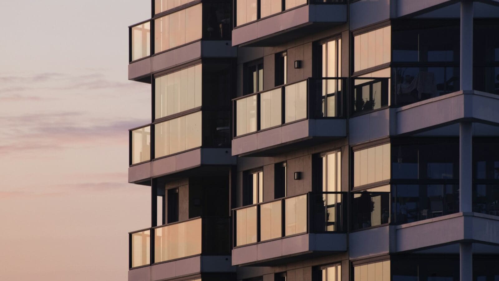 Modern apartment building facade with glass balconies reflecting a dusk sky